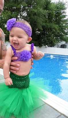 the baby is wearing a green and purple outfit with flowers on it's head