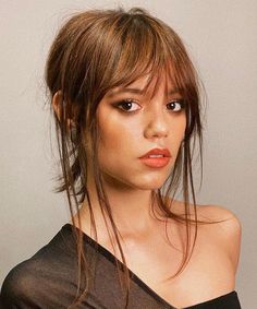 a woman in a black top posing for the camera with her hair pulled back into a bun