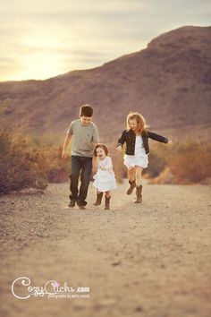 three children running down a dirt road with mountains in the background