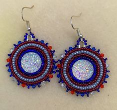 This item is a pair of beaded earrings. Made with size 11/0 red, blue and silver seed beads and a iridescent round resin rhinestone center. The edge beads are also red, blue and clear beads. Silver Beaded Round Earrings Gift, Silver Beaded Round Earrings For A Gift, Silver Beaded Earrings With Colorful Beads, Silver Round Beaded Earrings With Colorful Beads, Silver Round Earrings With Colorful Beads, Blue Round Beaded Earrings With Spacer Beads, Silver Beaded Crystal Earrings, Native American Beaded Earrings, Native American Beading