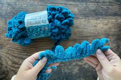 two hands holding blue yarn on top of a wooden table