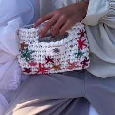 a woman's hand is holding a crocheted white purse with red and green decorations