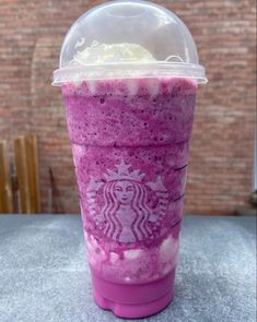 a purple drink with whipped cream in it on a table next to a brick wall