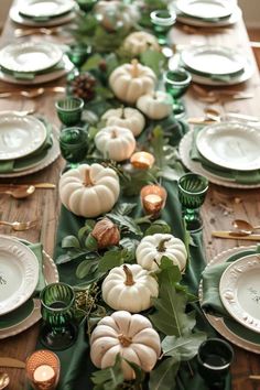 a long table with white pumpkins and greenery on the top, surrounded by green plates