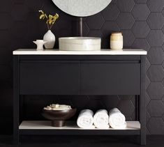 a bathroom with black walls and white towels on the shelf next to it is an oval mirror