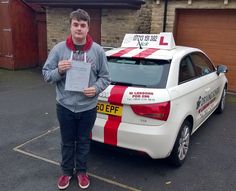 a man standing in front of a white car holding up a paper with the letter l on it