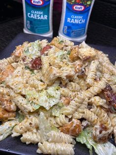 a black plate topped with pasta salad next to two bottles of ranch dressing