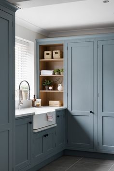 a kitchen with blue cupboards and white sink in the center, surrounded by wooden shelves