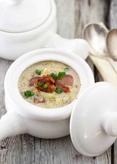 a white bowl filled with soup on top of a wooden table next to two spoons