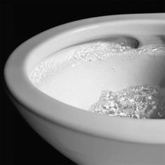 a white bowl filled with water on top of a black table next to a spoon