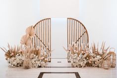 an arch decorated with flowers and plants in front of a white wall on the floor