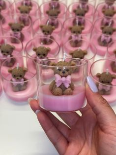 a hand holding a small candle with a teddy bear on it in front of rows of pink candles