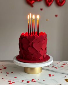 a red heart shaped cake with candles in the shape of hearts