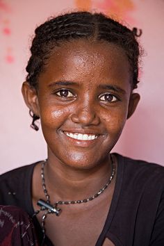 a woman with braids smiling at the camera while wearing a black shirt and necklace