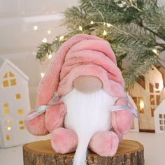 a pink and white stuffed animal sitting on top of a wooden stump next to a christmas tree