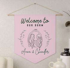 a welcome sign hangs on the wall next to a vase