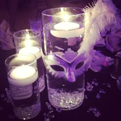 some candles are sitting on a table with purple flowers and white feathers in it,