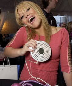 a woman laughing while holding a speaker in her right hand and headphones on her left