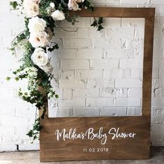 a wooden frame with white flowers and greenery on it, next to a brick wall