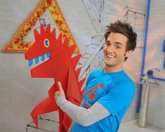 a young man holding up a paper cut out of a red dragon and pointing to it