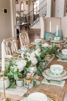 a dining room table set with plates and place settings, candlesticks and flowers