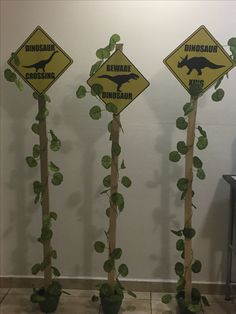 three signs with plants growing out of them in front of a wall that says dinosaur crossing and beware of dinosaurs