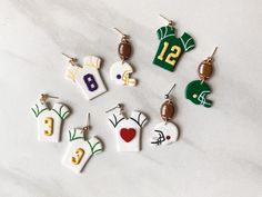 six different earrings with numbers on them sitting on a white surface, one has a football jersey and the other has a helmet