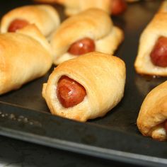 hotdogs wrapped in bread on a black tray with other food items behind them