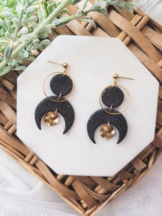 the black and gold earrings are sitting on top of a white table next to a plant