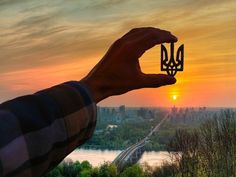 a person holding up a piece of paper with the sun setting in the distance behind them