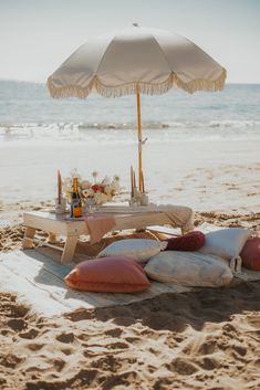 an umbrella is set up on the beach with pillows and drinks in front of it