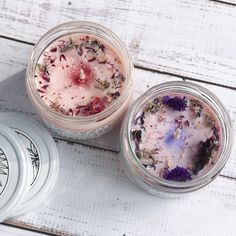 two jars filled with flowers sitting on top of a white wooden table next to each other