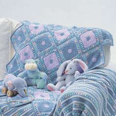 several stuffed animals sitting on a couch next to a crocheted blanket and pillow