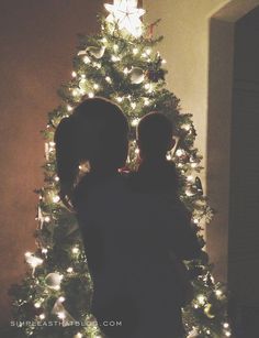 two people are standing in front of a christmas tree with lights on it and one person is holding the other's head