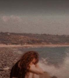 a woman sitting on top of a sandy beach next to the ocean