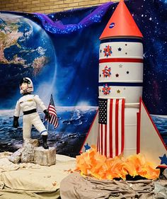 an astronaut statue next to a rocket and american flag in front of a wall mural