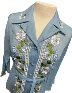 Really pretty vintage button up shirt with embroidered flowers on front, collar, and sleeves, and fabric covered buttons. Made of (I believe) a sheer muslin fabric with a nice sheen. Shirt has a matching fabric belt. Dates to around the 1970s and possibly made in China or Japan. Long sleeves widen at the wrist. Was found in the garage of an estate sale. It was hanging on a metal hanger and was very dirty. It cleaned up very well but does has a very faint rust stain remaining on shoulder and inside near collar. Please see photos with arrows. No holes or rips. The only label is the for the size. I'd say it fits like a medium but please FOLLOW MEASUREMENTS BELOW for the best fit. Would be beautiful paired with a white skirt or slacks or even jeans. **Please refer to the following measurements Fitted Embroidered Button-up Shirt, Fitted Embroidered Collared Shirt, Formal Shirt With Floral Embroidery For Spring, Spring Blouse With Covered Buttons And Spread Collar, Spring Shirt With Covered Buttons And Collar, Spring Cotton Shirt With Covered Buttons, Spring Shirt With Embroidered Spread Collar, Spring Shirt With Embroidery And Spread Collar, Spring Embroidered Shirt With Spread Collar