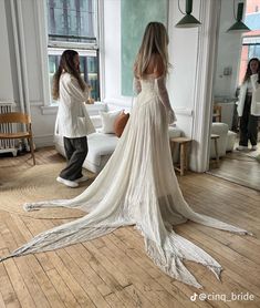 a woman in a white wedding dress standing on a wooden floor next to a window