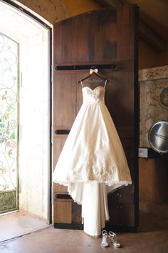 a wedding dress hanging on a rack in front of an open door with shoes nearby