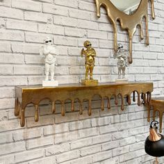 a white brick wall with gold paint dripping from it and two sculptures on the shelf