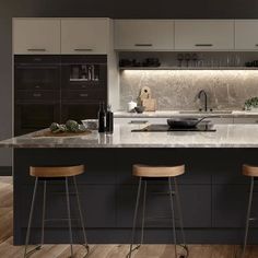 two stools sit in front of an island with marble countertops and black cabinets