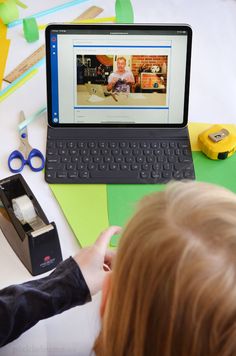 a child is playing with a laptop computer on the table next to scissors and tape