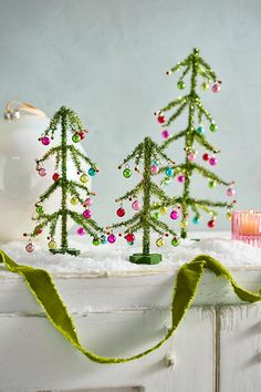 three small christmas trees sitting on top of a white shelf next to a candle holder