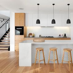 three stools sit in front of a kitchen island with stairs leading up to the second floor