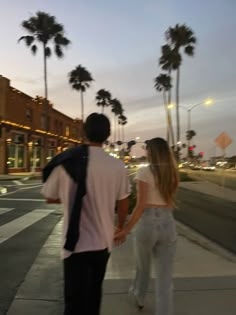 a man and woman walking down the sidewalk holding hands with palm trees in the background