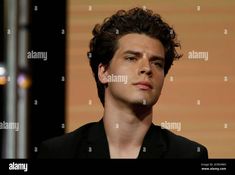 a young man with curly hair is looking at the camera while speaking on stage - stock image