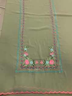 a green table cloth with pink and blue flowers on the border, sitting on top of a tile floor