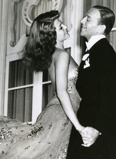 an old black and white photo of two people dressed in formal wear smiling at each other