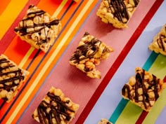 several pieces of dessert sitting on top of a colorful table cloth with chocolate drizzled over them