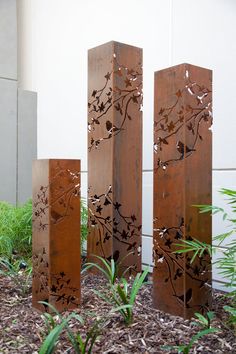 three tall metal sculptures sitting on top of a patch of dirt next to a building